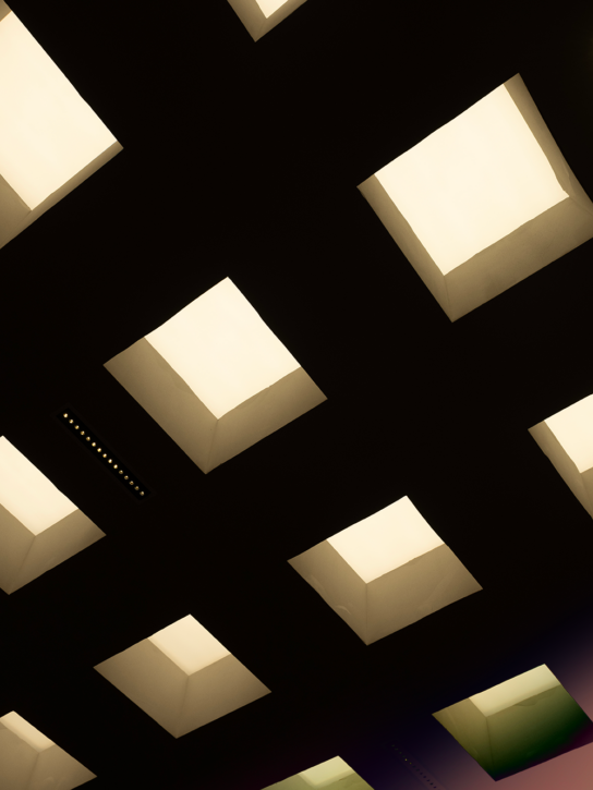 A modern ceiling with a pattern of square and rectangular lights emitting a soft glow.