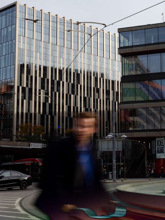 A busy city street in Stockholm with modern buildings and a blurred person walking in the foreground.