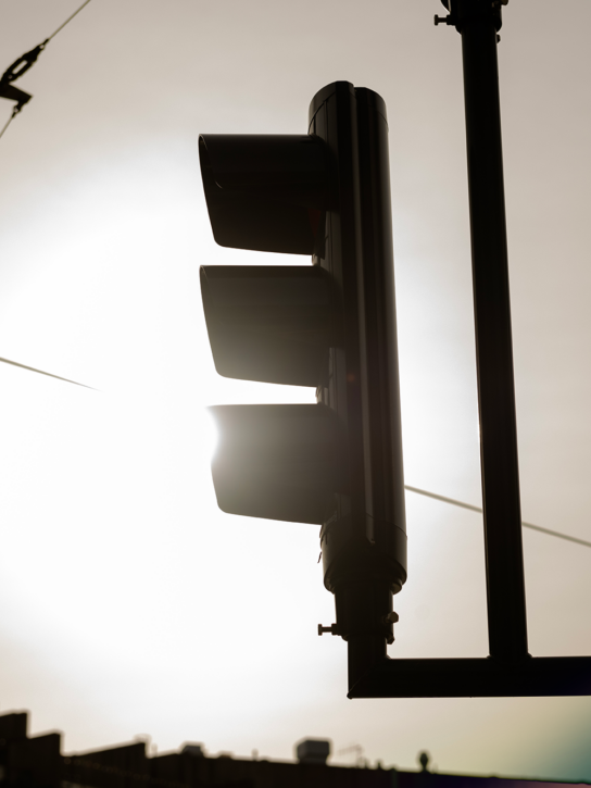 A traffic light in silhouette against a bright sky with lens flare.