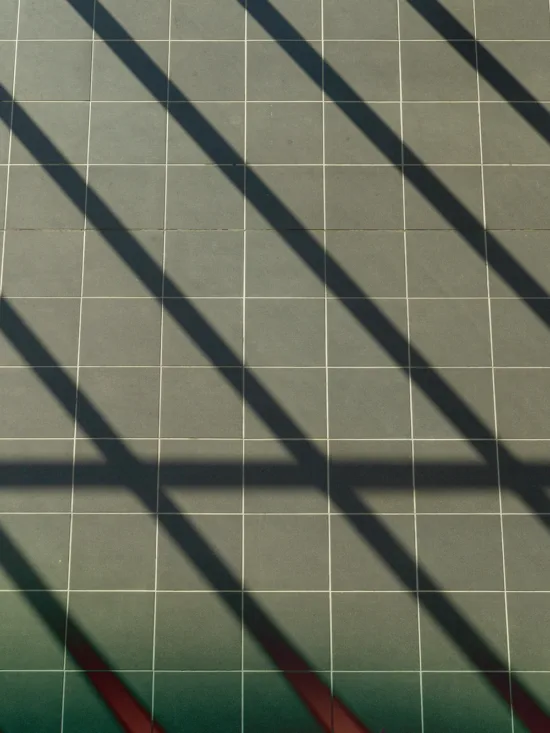 A tiled floor with diagonal shadows from a railing or fence.