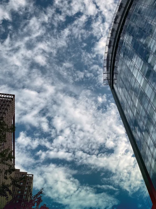 A tall building with a curved glass facade reflecting the sky and clouds.