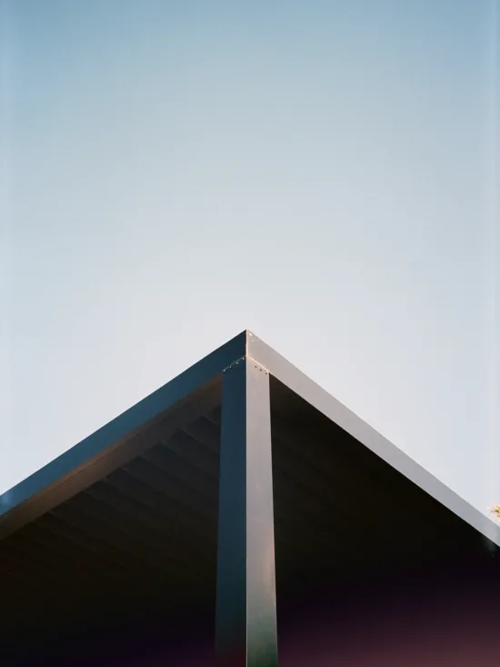 A dark triangular roof corner against a clear, blue sky.