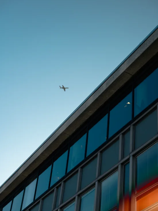 A modern building and an airplane flying in the clear blue sky above it.