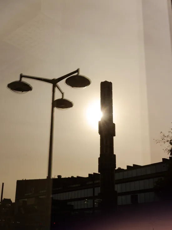 A cityscape silhouette with two street lamps and a bright sun in the sky, creating a contrast of light and shadow.