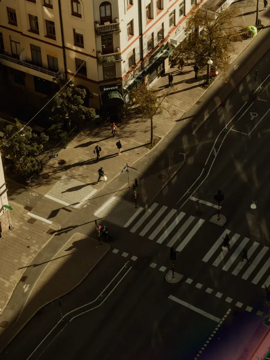 Top-down view of a city street intersection with pedestrians crossing, vehicles, and buildings.