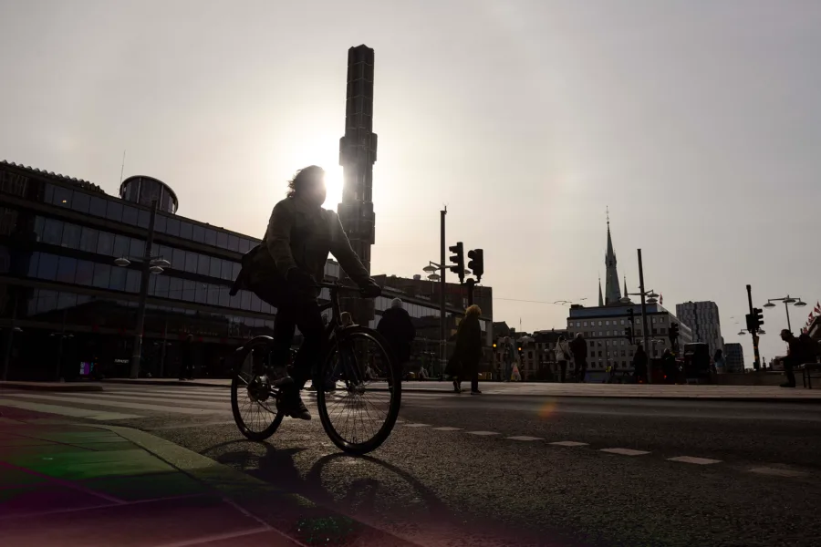 A silhouette of a person on a bicycle in a city street with buildings and a tall tower in the background.