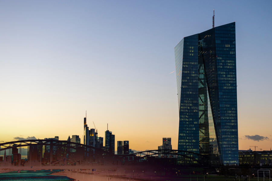 A modern skyscraper with a curved glass facade at sunset, with several buildings in the background.