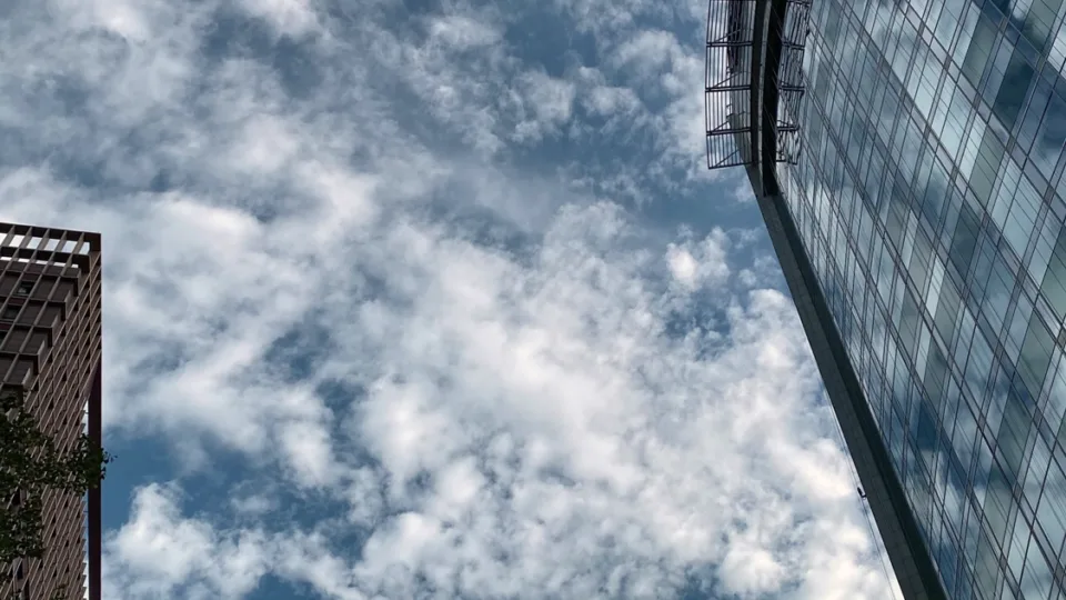 A tall building with a curved glass facade reflecting the sky and clouds.
