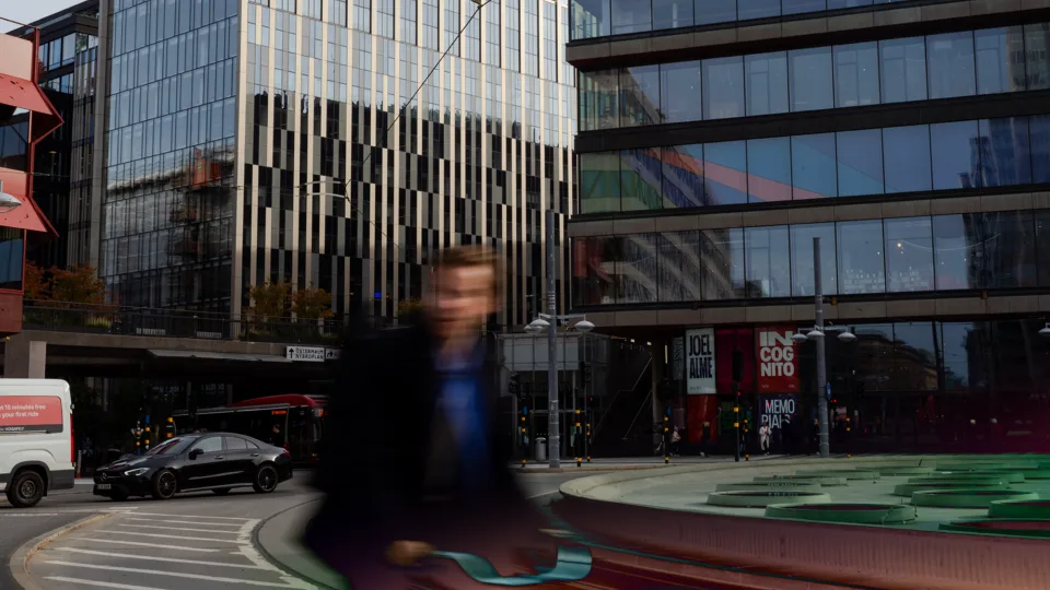 A busy city street in Stockholm with modern buildings and a blurred person walking in the foreground.