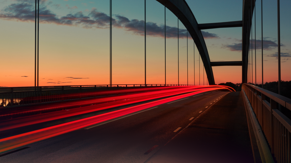 A bridge at sunset with red and white light trails from passing cars.