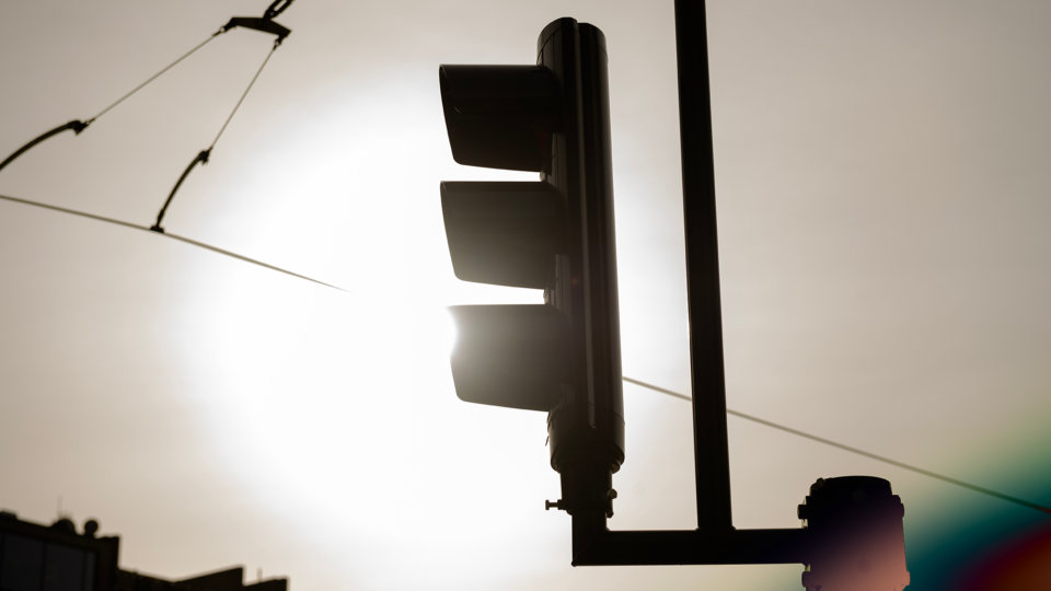 A traffic light in silhouette against a bright sky with lens flare.