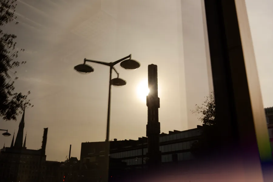 A cityscape silhouette with two street lamps and a bright sun in the sky, creating a contrast of light and shadow.