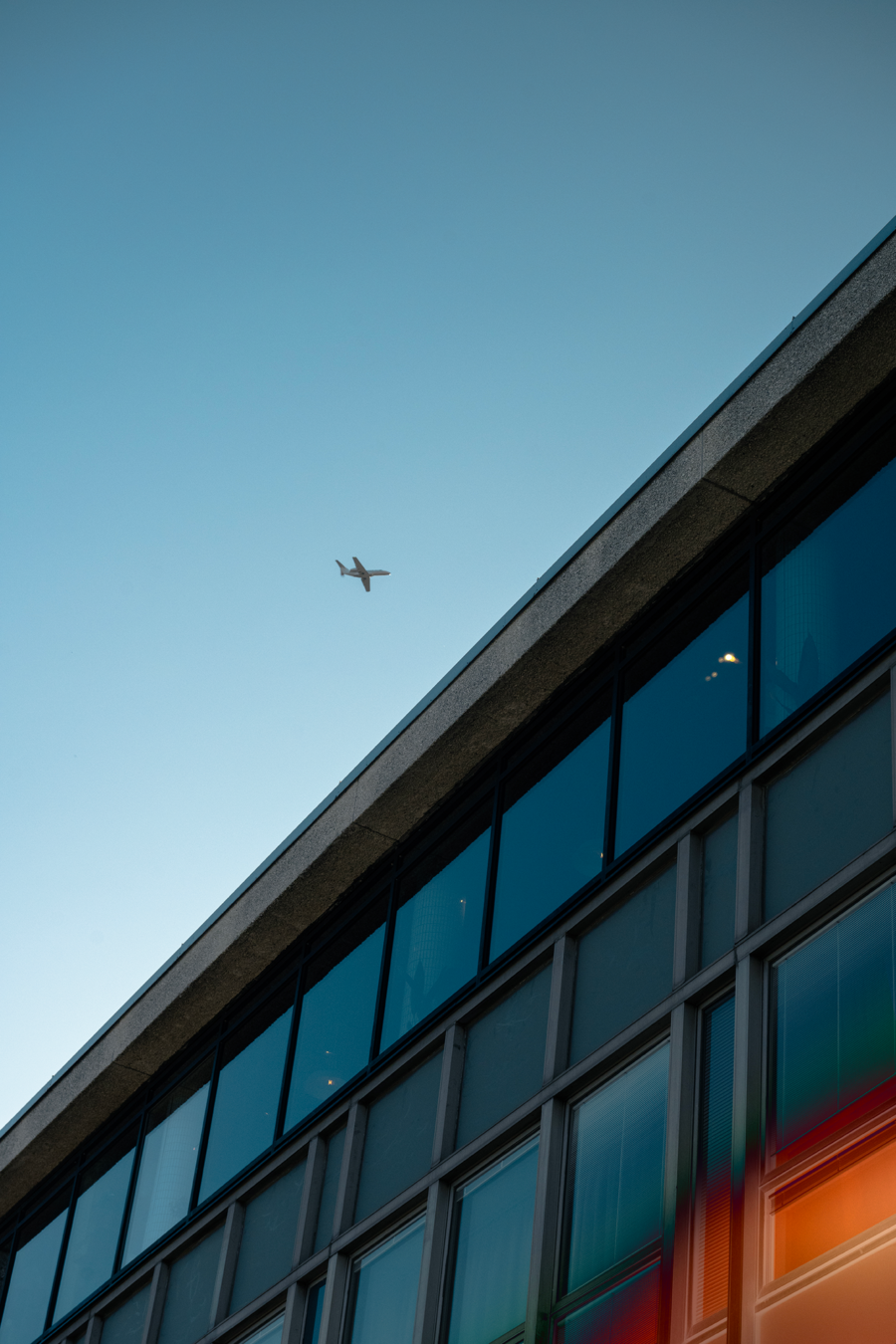 A modern building and an airplane flying in the clear blue sky above it.