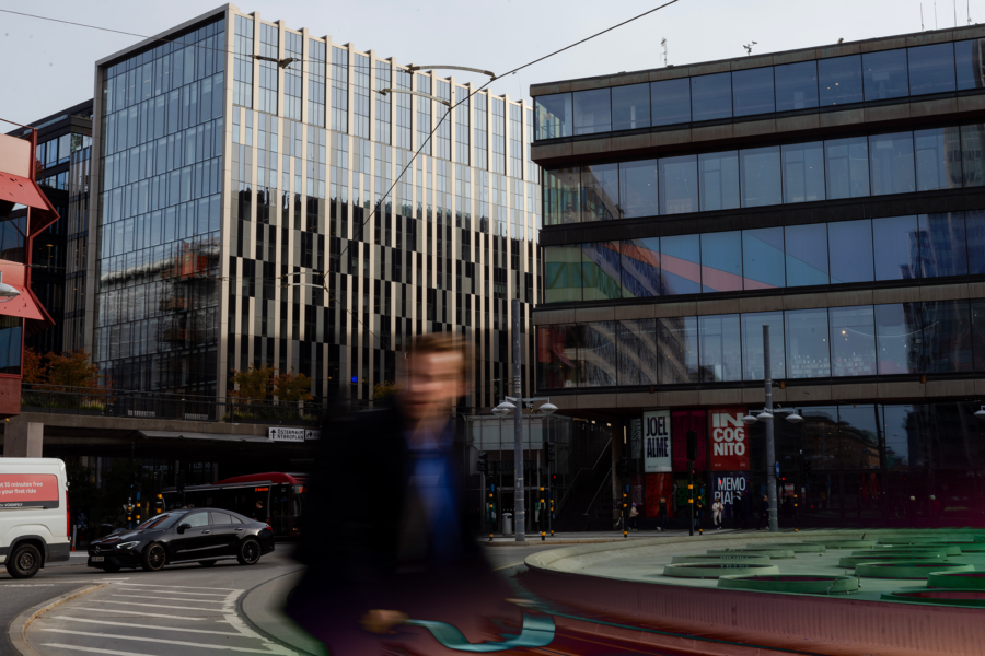 A busy city street in Stockholm with modern buildings and a blurred person walking in the foreground.