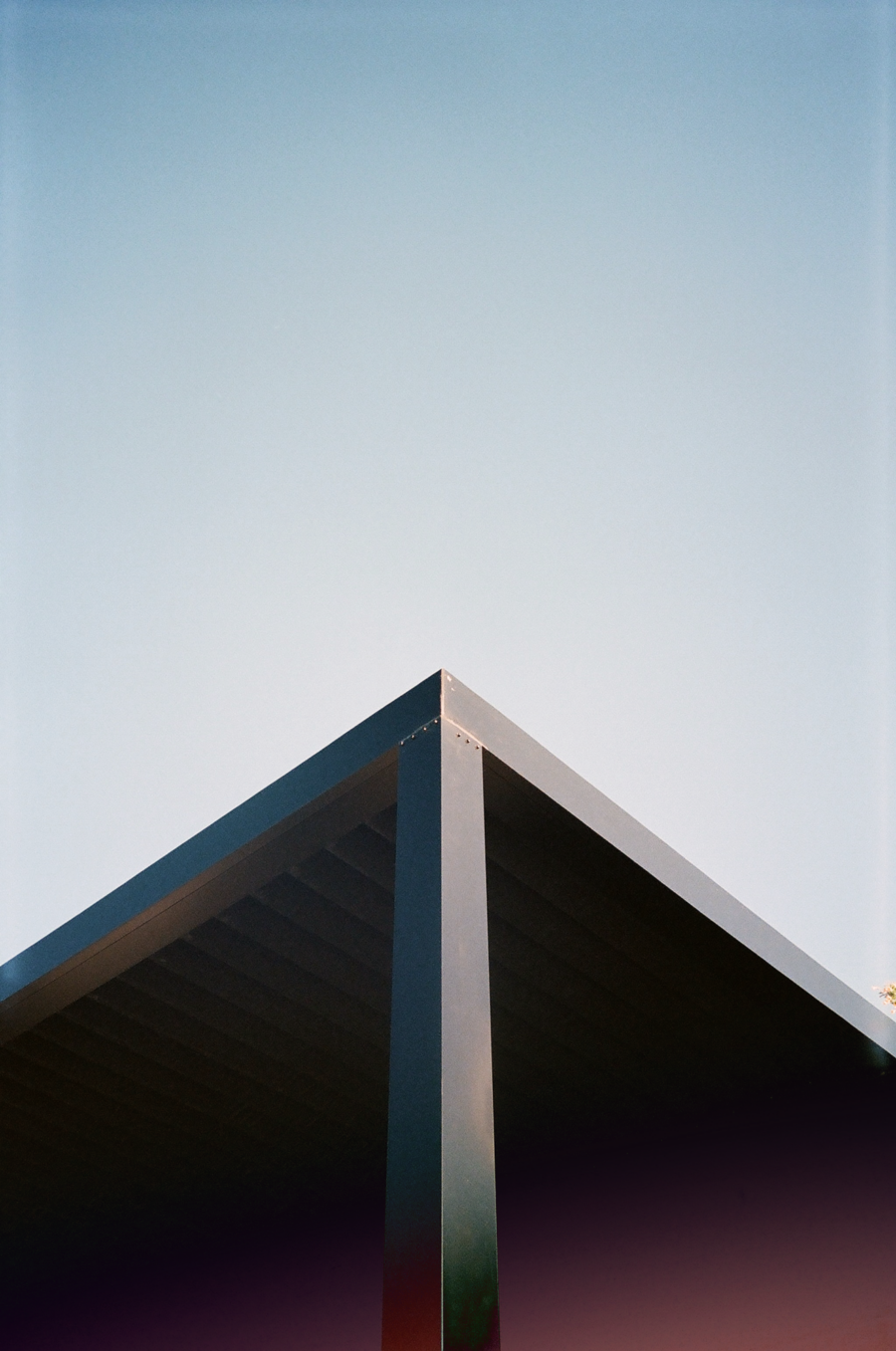 A dark triangular roof corner against a clear, blue sky.