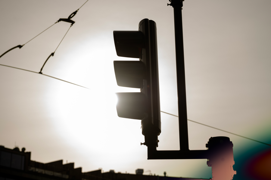 A traffic light in silhouette against a bright sky with lens flare.