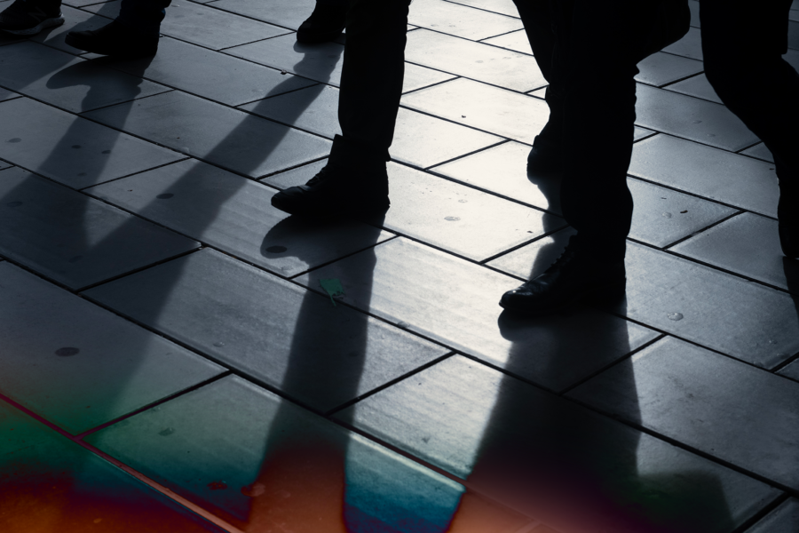 Silhouetted figures casting shadows on a tiled floor, with a colorful light reflection.