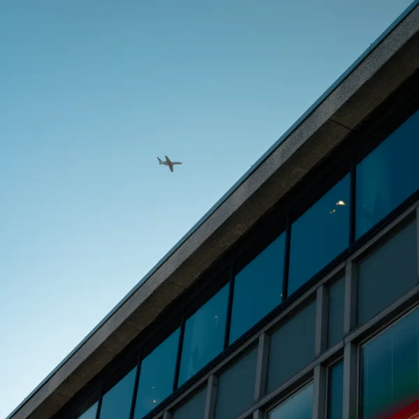 A modern building and an airplane flying in the clear blue sky above it.