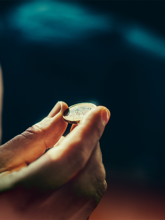 Focused view of a hand holding a coin, with blurred dark background.
