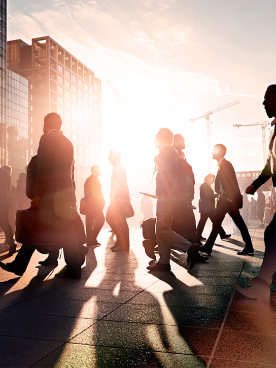 Silhouetted figures walking on a bustling city street at sunset, with tall modern buildings and a vibrant sunset.
