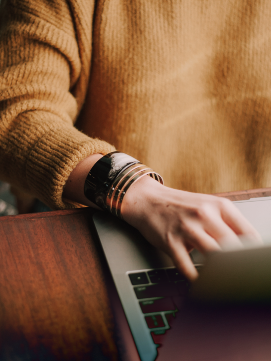 A person in a mustard colored sweater working on a laptop.