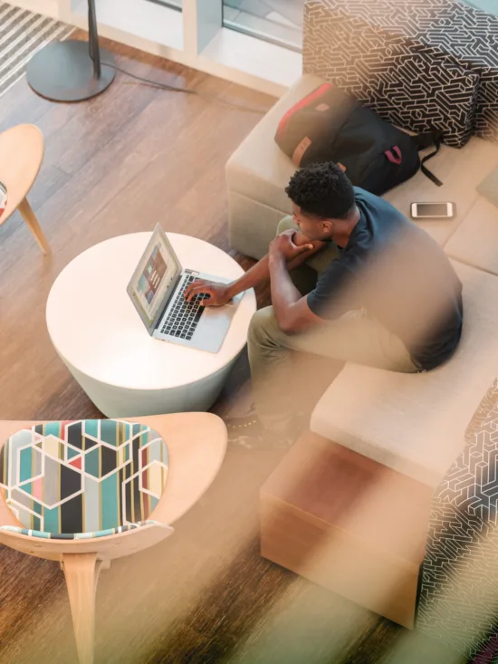 Person working on laptop in modern living room with gray couch, white coffee table, and natural light.