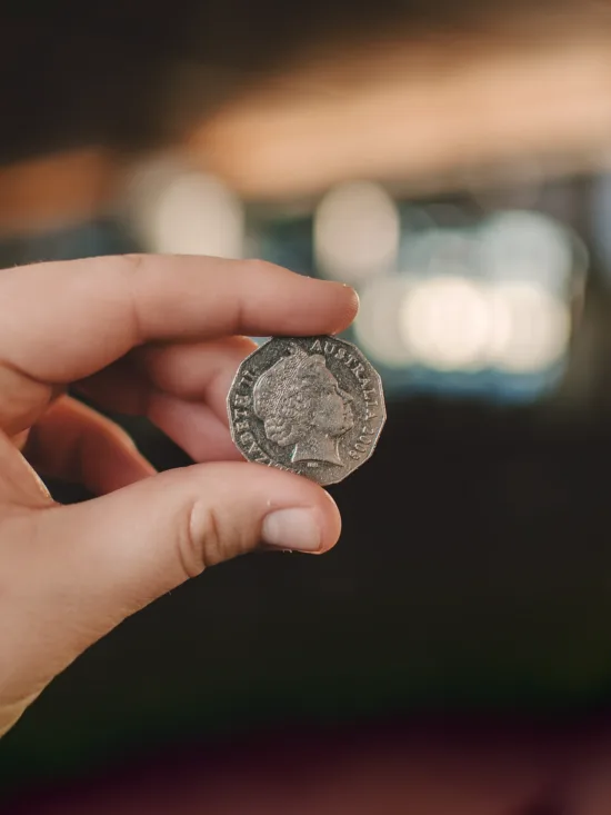 Hand holding a silver coin, against a blurred indoor background.