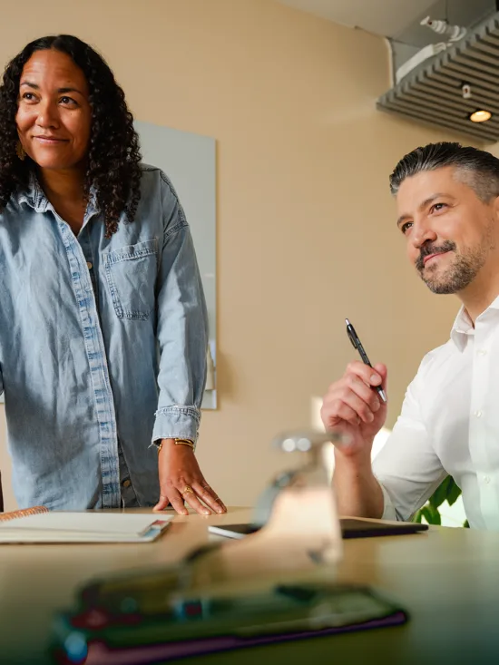 Two people in a modern office, one standing and the other seated, engaged in a discussion.