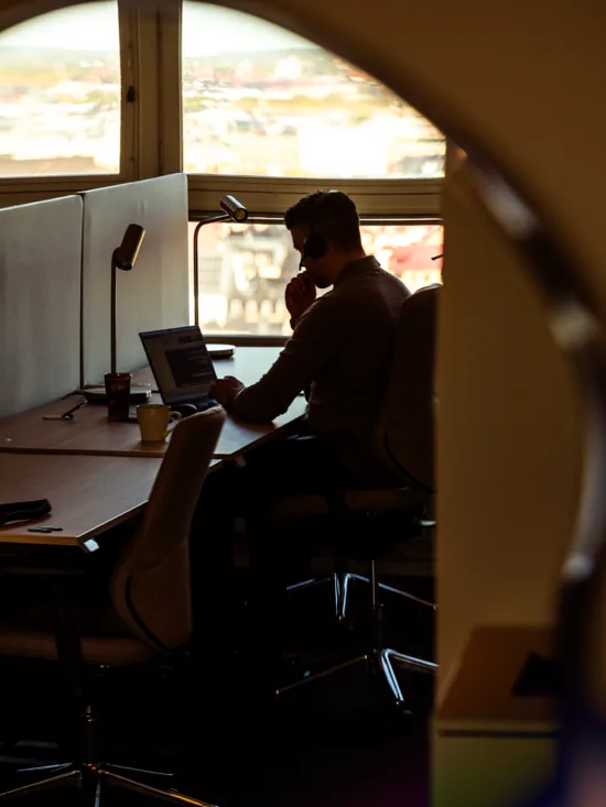 A silhouette of a person working at a desk with a computer and other equipment, seen through a circular window. 