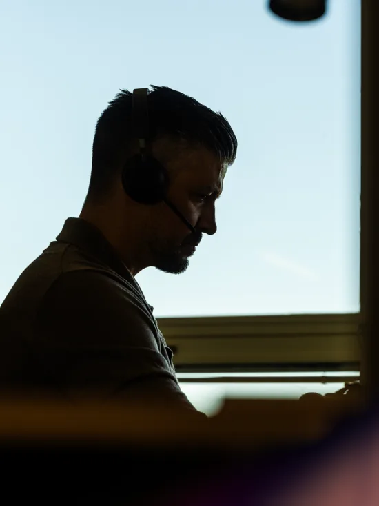 A man sitting by a window attending an online meeting on his lapop.