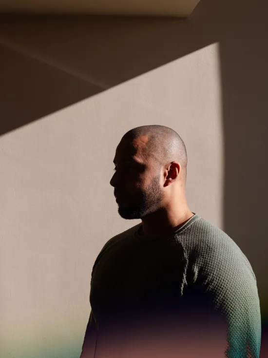 A person wearing a green sweater stands in front of a beige wall.