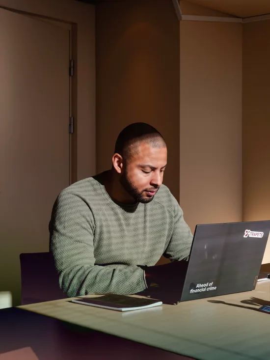 Man in a green sweater working on a laptop at a wooden desk with office supplies.