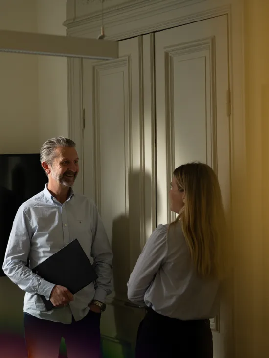 Two people standing in a meeting room with a blurred background.