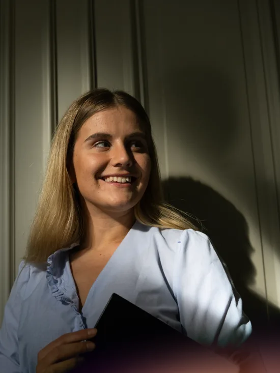 A smiling woman with blonde hair, holding a laptop.