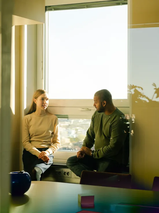 Two people sitting next to a window, in a brightly lit office.