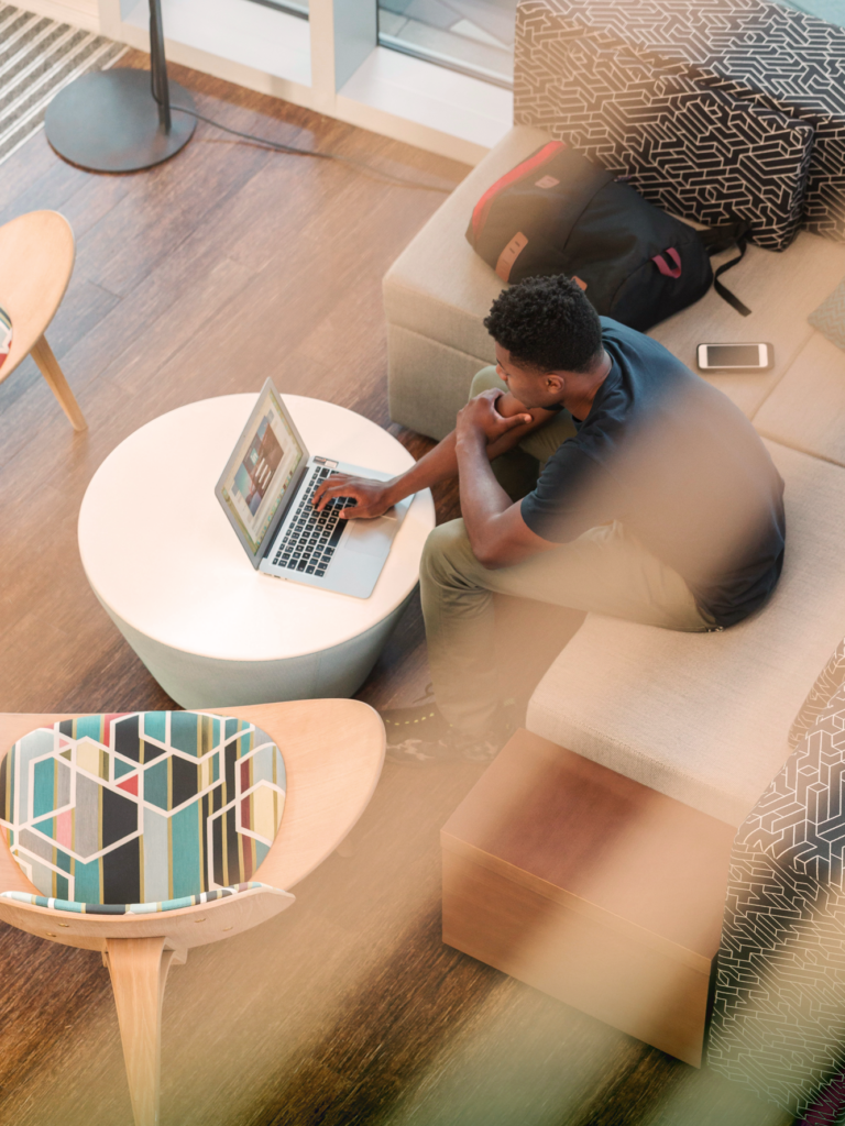 Person working on laptop in modern living room with gray couch, white coffee table, and natural light.