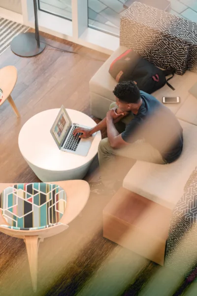 Person working on laptop in modern living room with gray couch, white coffee table, and natural light.