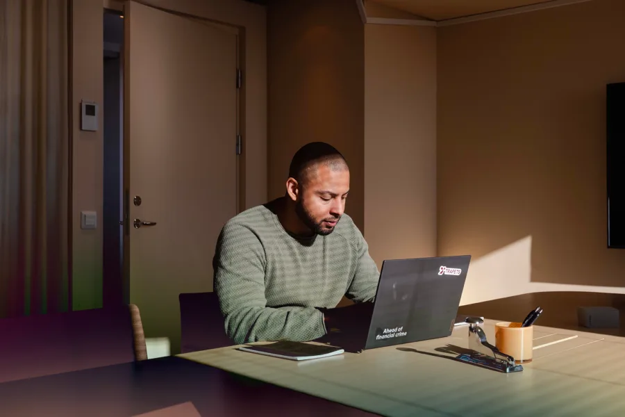 Man in a green sweater working on a laptop at a wooden desk with office supplies.
