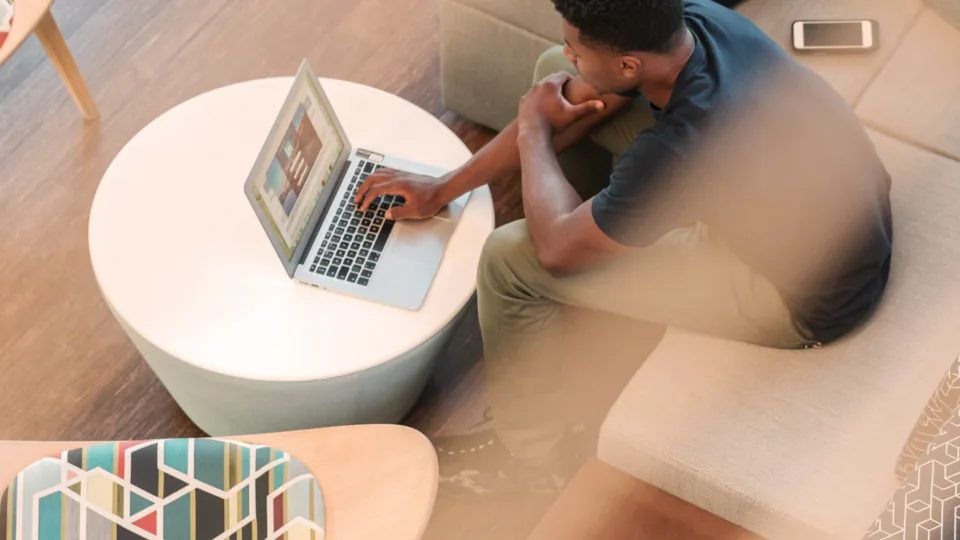 Person working on laptop in modern living room with gray couch, white coffee table, and natural light.