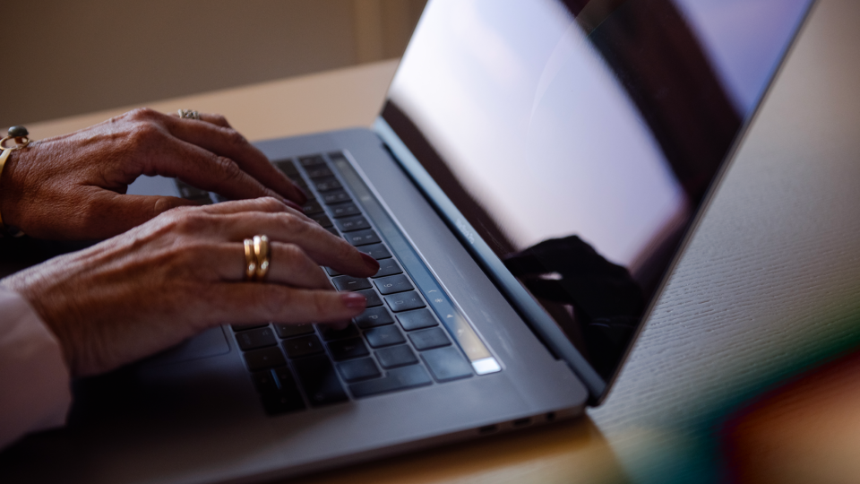 Close-up view of hands wearing a gold ring and a watch, typing on a silver laptop keyboard.