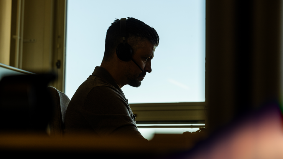 A man sitting by a window attending an online meeting on his lapop.