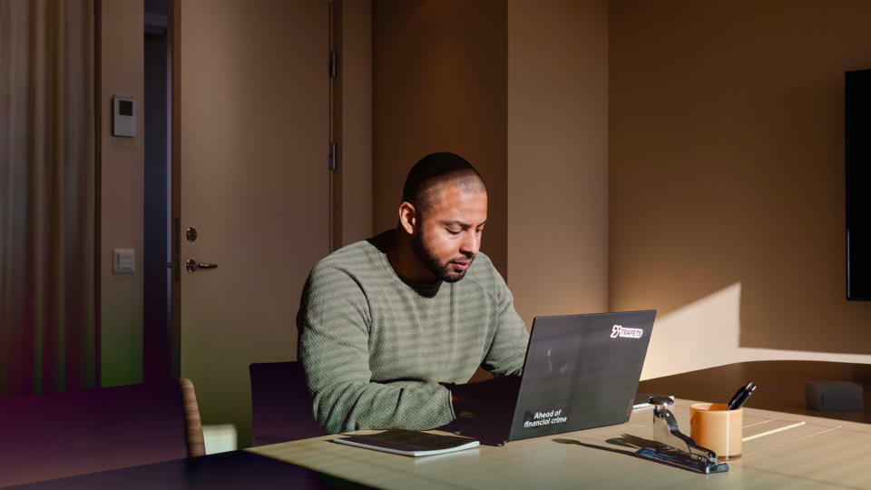 Man in a green sweater working on a laptop at a wooden desk with office supplies.