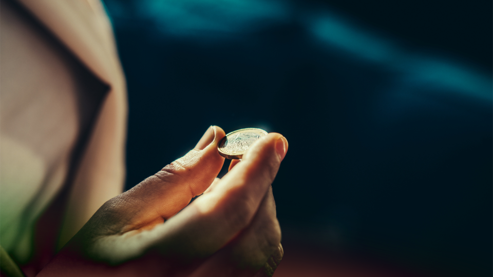 Focused view of a hand holding a coin, with blurred dark background.