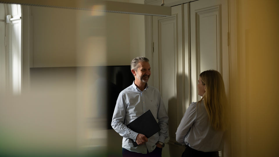 Two people standing in a meeting room with a blurred background.
