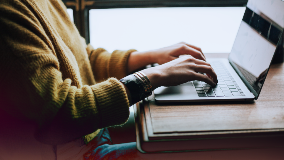 A person with a yellow sweater typing on a laptop.