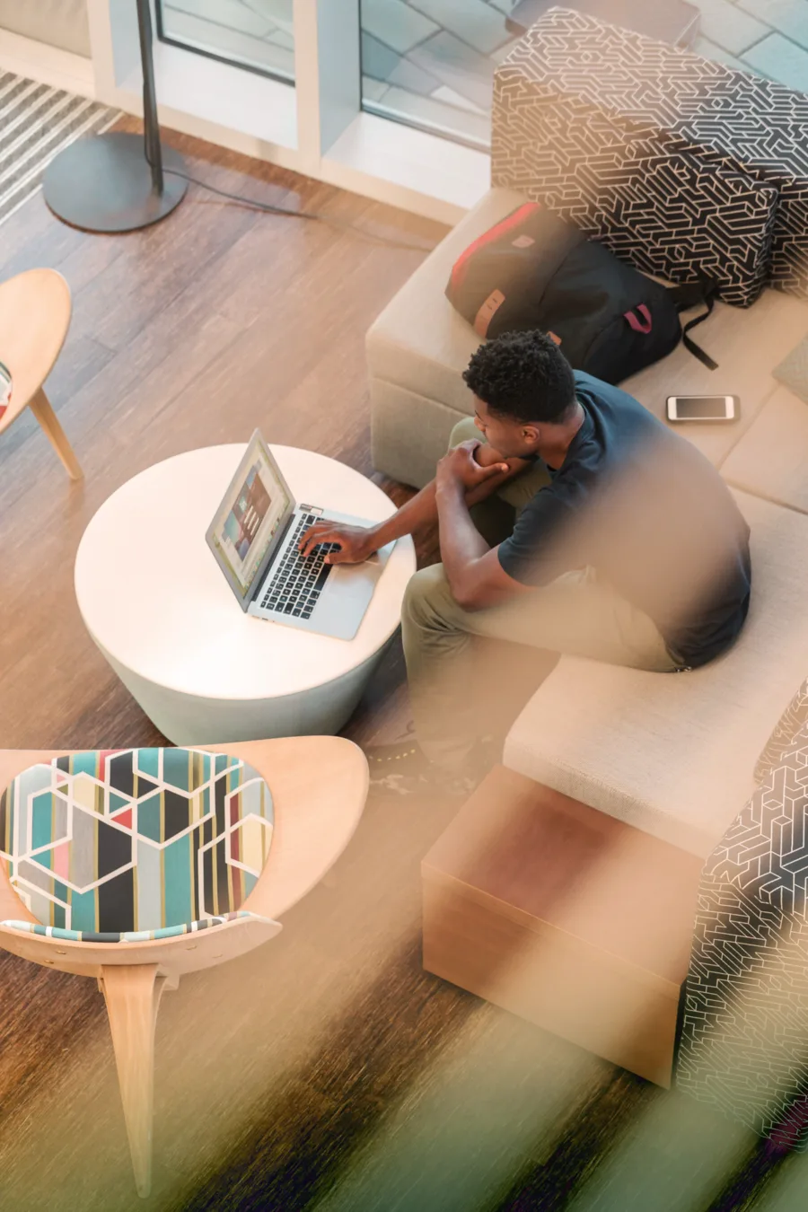 Person working on laptop in modern living room with gray couch, white coffee table, and natural light.