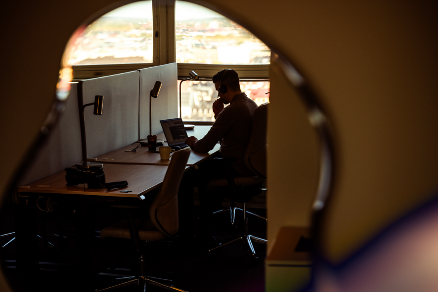 A silhouette of a person working at a desk with a computer and other equipment, seen through a circular window. 