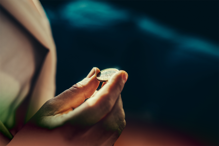 Focused view of a hand holding a coin, with blurred dark background.