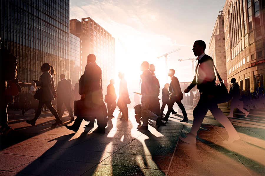 Silhouetted figures walking on a bustling city street at sunset, with tall modern buildings.