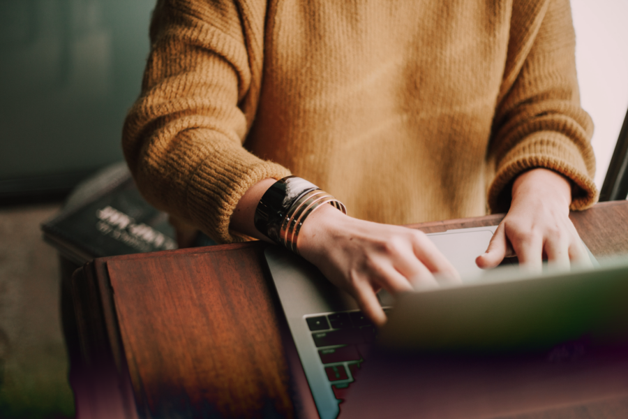 A person in a mustard colored sweater working on a laptop.